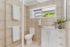 Een badkamer met toilet, wastafel en kast, een raam met uitzicht op groen, en een handdoekhouder.