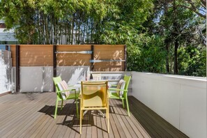 En balkon med trægulv, et bord med stole og en hvid væg.