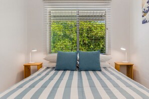 A bedroom with a bed, two bedside tables, and a window with blinds. - Kareela Court 4 Kareela Avenue 14 (Noosa Heads)