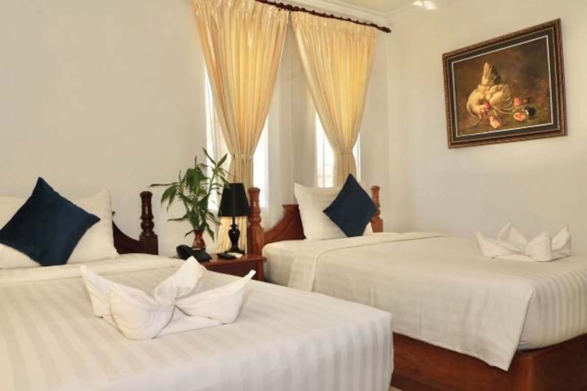 Una habitación de hotel con dos camas, un cuadro en la pared y una ventana con cortinas.