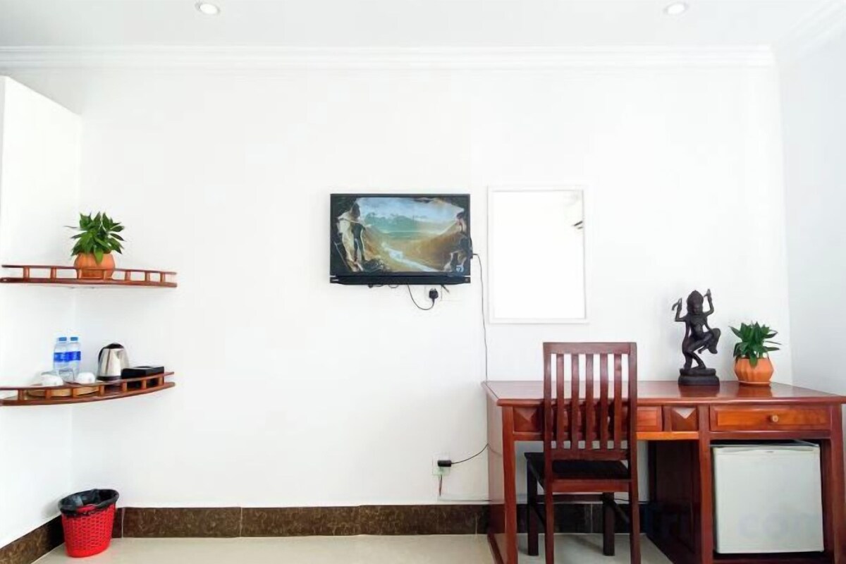 Une pièce comprenant un bureau en bois, une chaise et un téléviseur fixé au mur.