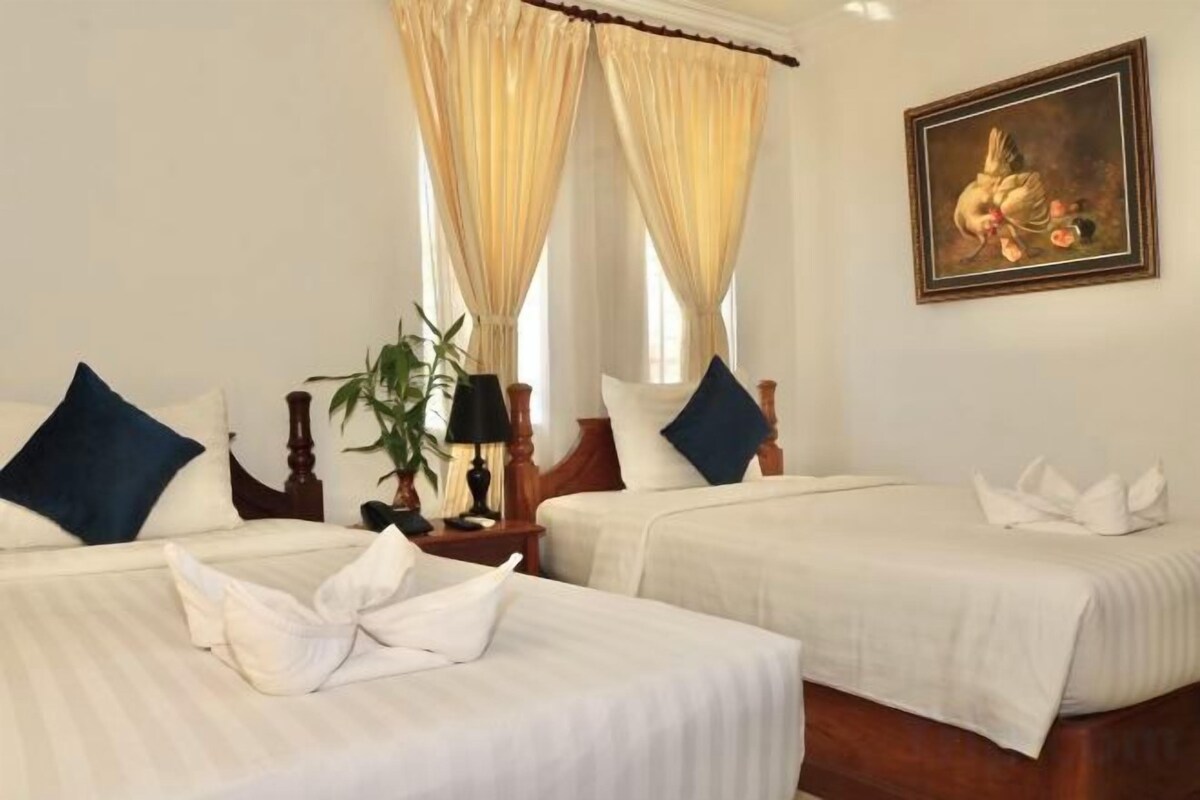 A hotel room with two beds, a painting on the wall, and a window with curtains.