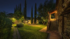 A well-lit garden with a stone pathway leading to a wooden house with a staircase. - Podere Caprarecce 8, Emma Villas (Baccinello)