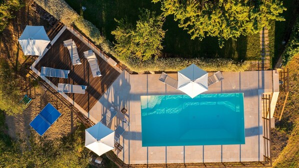 An aerial view of a swimming pool area with a deck, lounge chairs, and umbrellas.