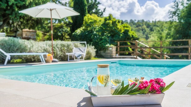 A poolside setting with a clear pool, lounge chairs, and a table with a pitcher of water and flowers. - Podere Caprarecce 8, Emma Villas (Baccinello)