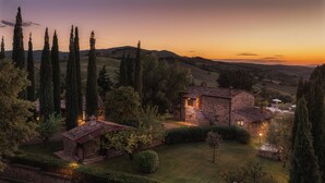 A stone house with a tiled roof, surrounded by a well-maintained garden and tall cypress trees. - Podere Caprarecce 8, Emma Villas (Baccinello)