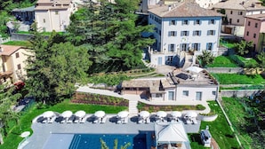 A residential area with a large building featuring a swimming pool, outdoor seating, and a garden. - Villa Cappelletti 16+2, Emma Villas (Corgneto)