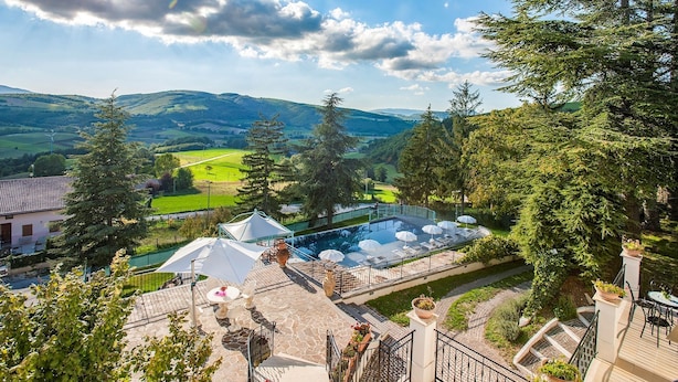 A pool area with a view of the countryside, surrounded by trees and a building with a tiled roof. - Villa Cappelletti 16+2, Emma Villas (Corgneto)