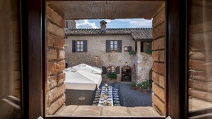 A courtyard with a long table set for dining, stone walls, and a tiled roof.