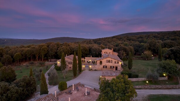 A stone villa with a central courtyard, surrounded by trees and hills.