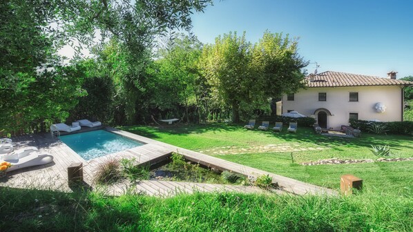 A pool with lounge chairs, a garden with a pergola, and a villa with a tiled roof.