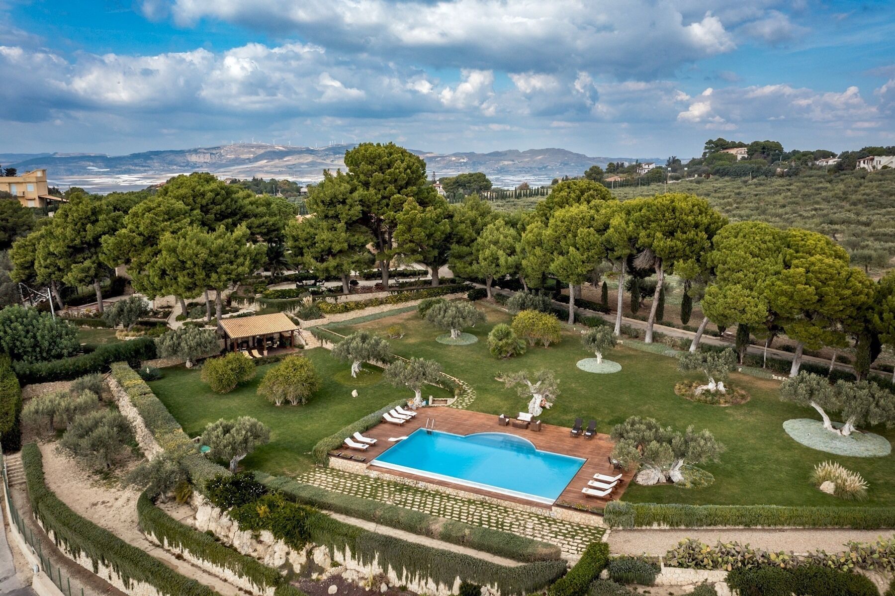 Propiedad ajardinada con piscina, áreas verdes y vistas a colinas distantes.