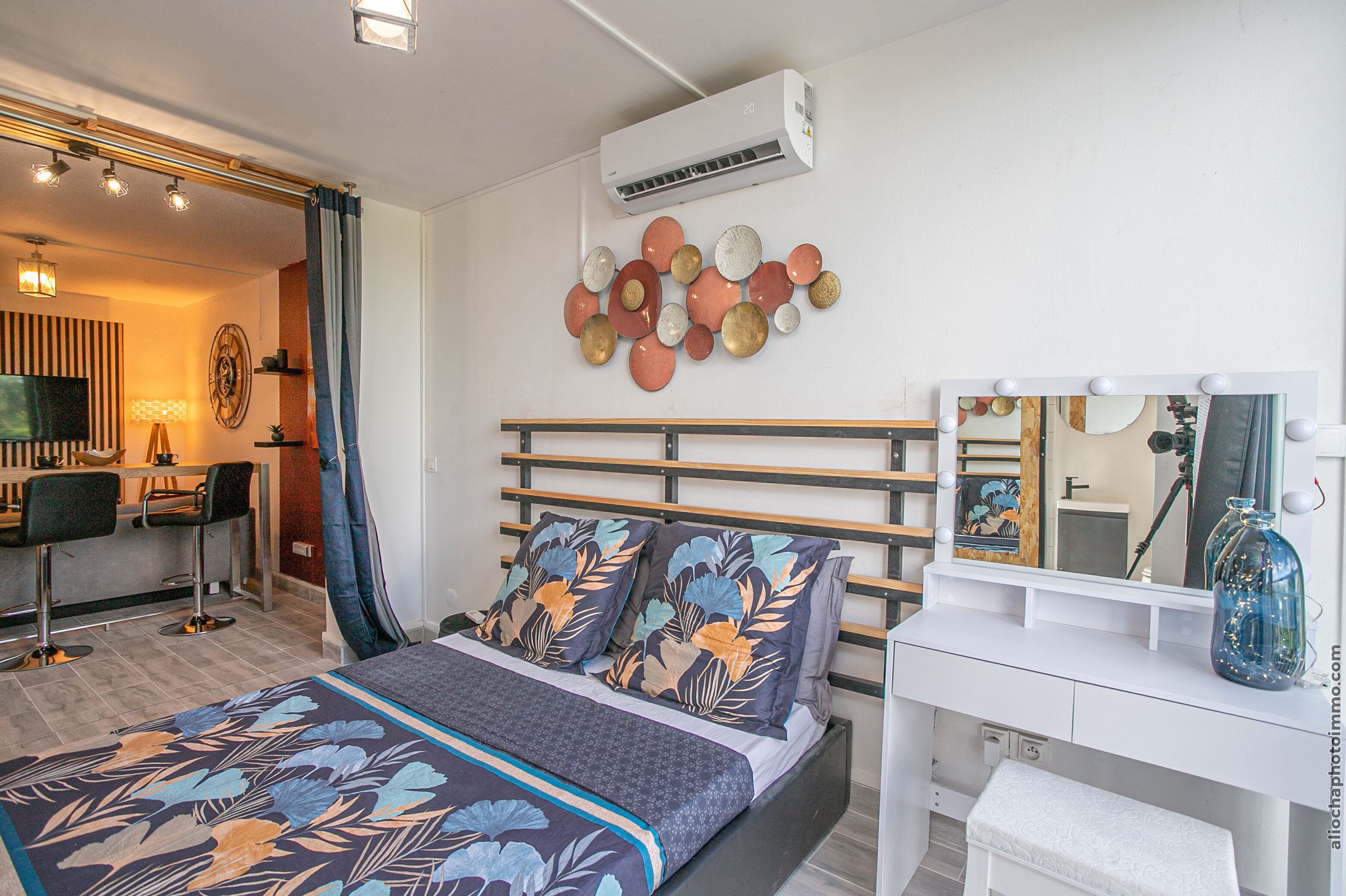 A modern bedroom with a bed, a vanity with a mirror, and a wall-mounted air conditioner.
