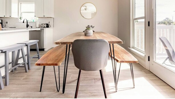 Une cuisine moderne avec des meubles blancs, une table à manger en bois avec des bancs, et une grande fenêtre offrant une vue sur l’extérieur.