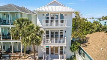 A two-story beachfront house with a balcony on the second floor, a covered porch, and a small deck area.
