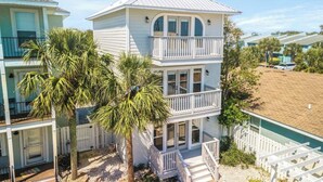 A two-story beachfront house with a balcony, palm trees, and a sandy beach in the background. - Modern Poolside villa: Steps to the sand, modern comforts, ultimate relaxation (Panama City Beach)