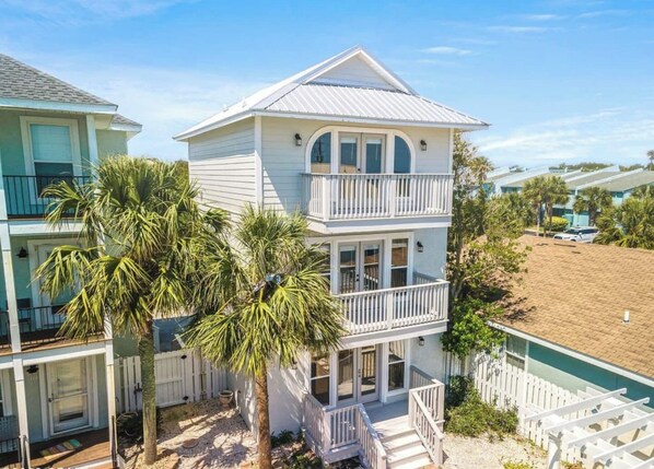 A two-story beachfront house with a balcony, palm trees, and a sandy beach in the background. - Modern Poolside villa: Steps to the sand, modern comforts, ultimate relaxation (Panama City Beach)