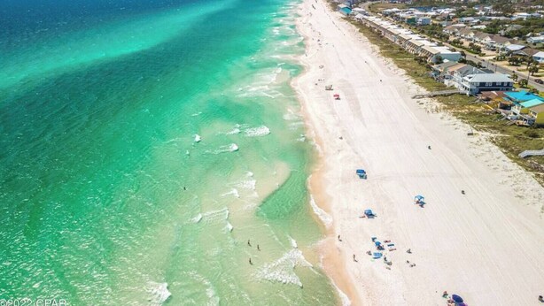 An aerial view of a beach with clear turquoise waters, a sandy shore, and a row of buildings along the coastline. - Modern Poolside villa: Steps to the sand, modern comforts, ultimate relaxation (Panama City Beach)