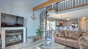 A spacious living room with a fireplace, a comfortable sofa, a glass coffee table, and a wooden staircase leading to an upper level. - Lakefront Retreat: Prime Osage Beach Location! (Osage Beach)