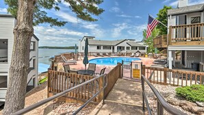 A pool area with a view of a lake, wooden deck, and a flag. - Lakefront Retreat: Prime Osage Beach Location! (Osage Beach)