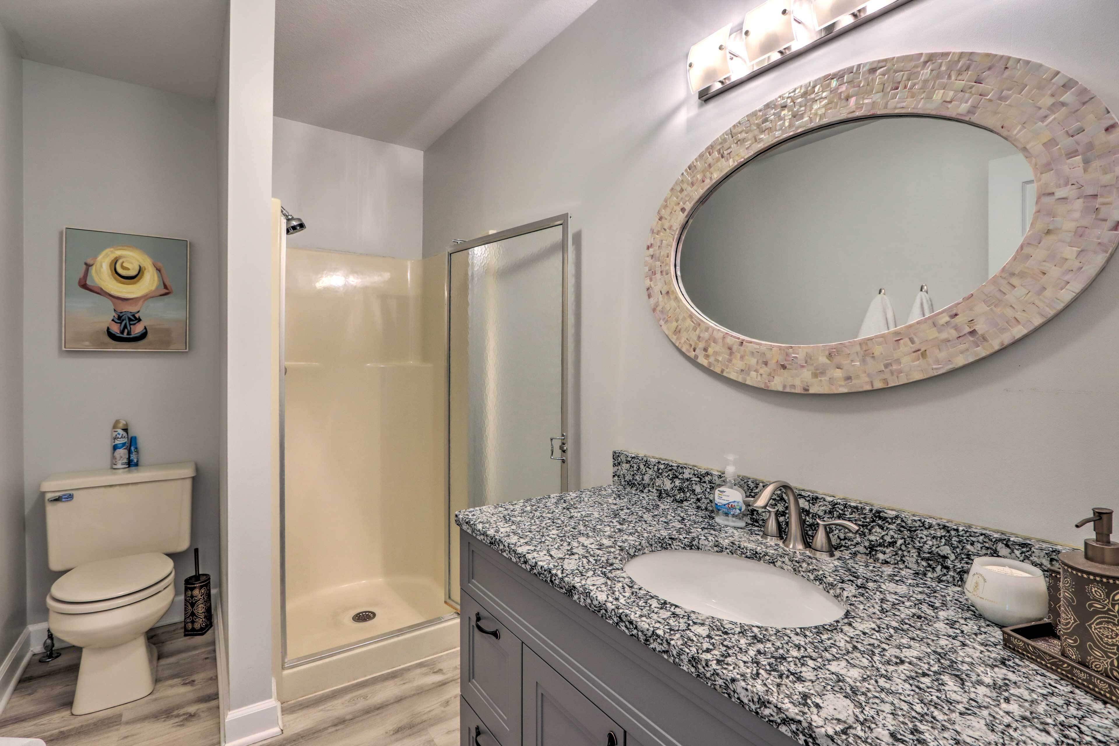 Un baño con inodoro, ducha, lavamanos y un espejo grande con detalles de mosaico.