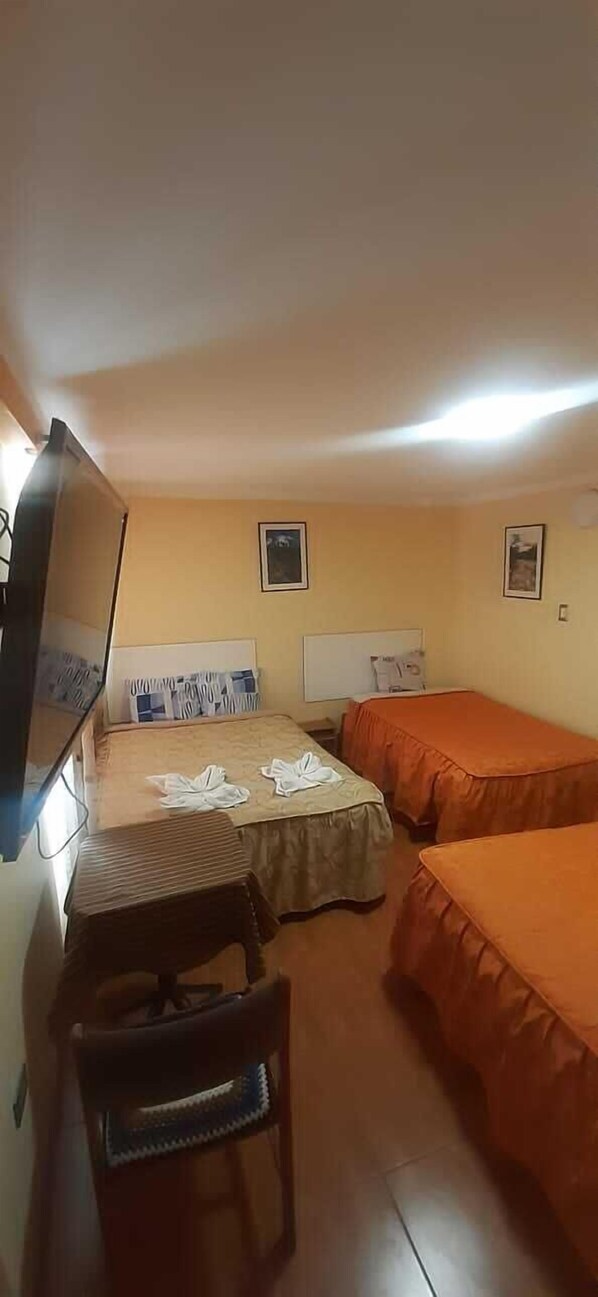 Une petite chambre d’hôtel composée d’une seule pièce, avec deux lits, un bureau et une chaise.