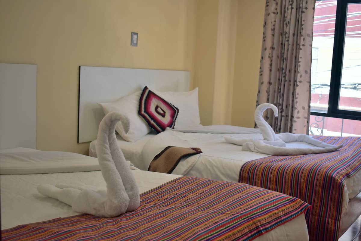 Habitación de hotel con dos camas, cada una con cabecera blanca, cubrecama a rayas de colores y almohada decorativa.