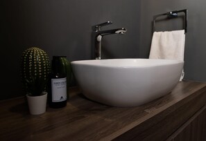 Ein Badezimmer mit weißem Waschbecken, Wasserhahn, Handtuchhalter und einer Topfpflanze.