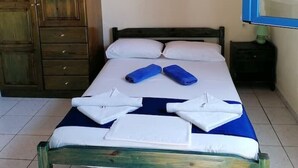A single bed with white and blue linens, a wooden wardrobe, and a blue-framed mirror. - "Eothinos" Sea front Studio (Glossa Skopelos Island,)