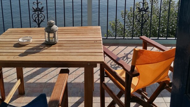 Ein Holztisch mit einer Laterne und einer Schüssel, ein Holzsessel und Blick auf das Meer mit Segelbooten.