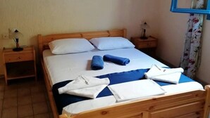 Ein hölzernes Bett mit blauer Bettdecke und weißen Laken, zwei Nachttische mit Lampen sowie eine wandmontierte Klimaanlage.