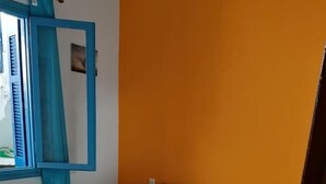 Un lit simple avec du linge de lit blanc et bleu, une tête de lit en bois et un rideau bleu.
