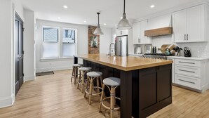 Una cocina moderna con una isla grande, taburetes de bar, armarios blancos y una pared decorativa de ladrillo.