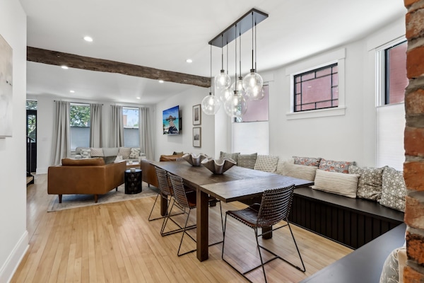 Open and airy living room with elegant seating, a dining table, chandelier lighting, and large windows creating a warm and inviting space for gatherings.