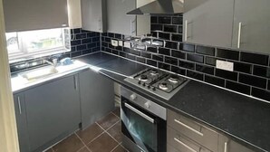 A compact kitchen with grey cabinets, a black tiled backsplash, a gas stove, and a built-in oven. - 4 bed Townhouse- Free parking (Greater London)