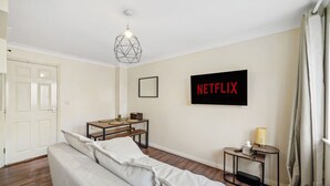 A modern living room with a sofa, a small table, a wall-mounted TV, and a geometric light fixture. - 4 bed Townhouse- Free parking (Greater London)