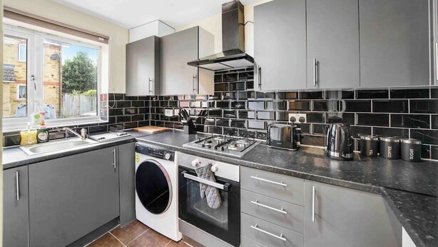 A modern kitchen with grey cabinets, a built-in oven, a washing machine, and a coffee maker.