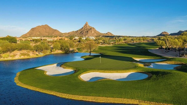 Un campo de golf con un obstáculo acuático, búnkeres de arena y un mástil con bandera.