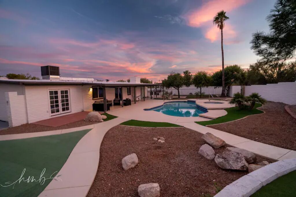 A backyard with a swimming pool, a patio area, and a house.