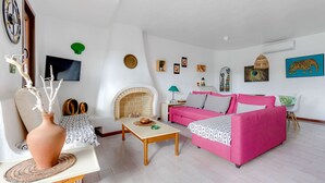 Ein Wohnzimmer mit einem rosafarbenen Sofa, einem weißen Sessel, einem Holztisch, einem Fernseher und einem Kamin.
