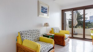 Ein modernes Wohnzimmer mit einer Couch und Sesseln, einem kleinen Tisch mit einer Lampe und einer großen Glasschiebet ür, die zu einem Außenbereich führt.
