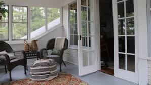 A cozy room with wicker furniture, a patterned ottoman, and a view of the outdoors through large windows. - Lakeview Historic Home Guest Rave: Delicious Breakfast  (Wisconsin Dells)