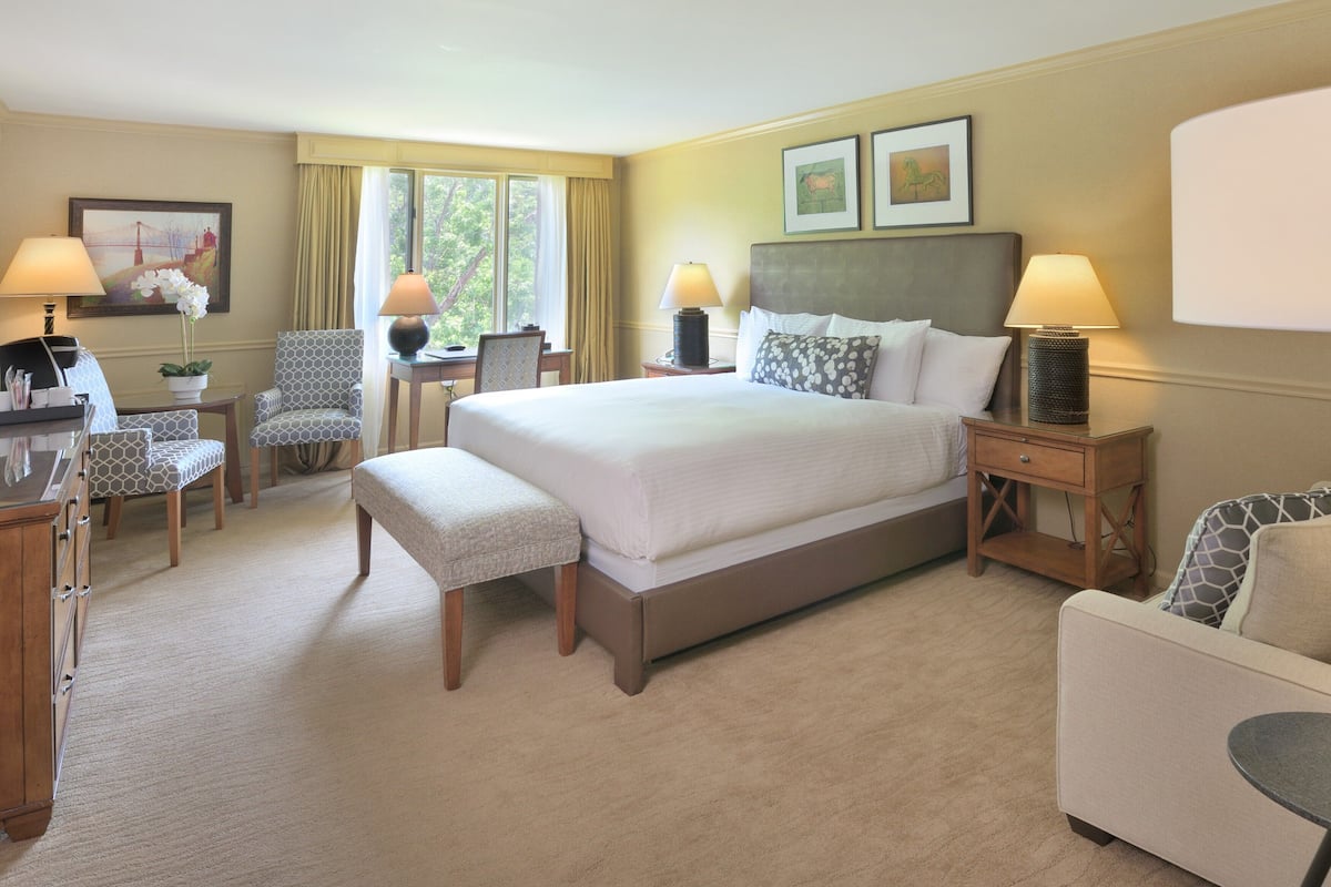 Ein Hotelzimmer mit einem großen Bett, zwei Nachttischen, einem Schreibtisch, einem Sessel und einem kleinen runden Tisch.