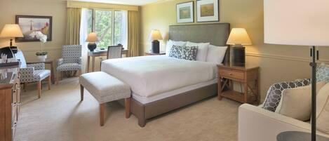 A hotel room with a large bed, two bedside tables, a desk, a chair, and a small round table.
