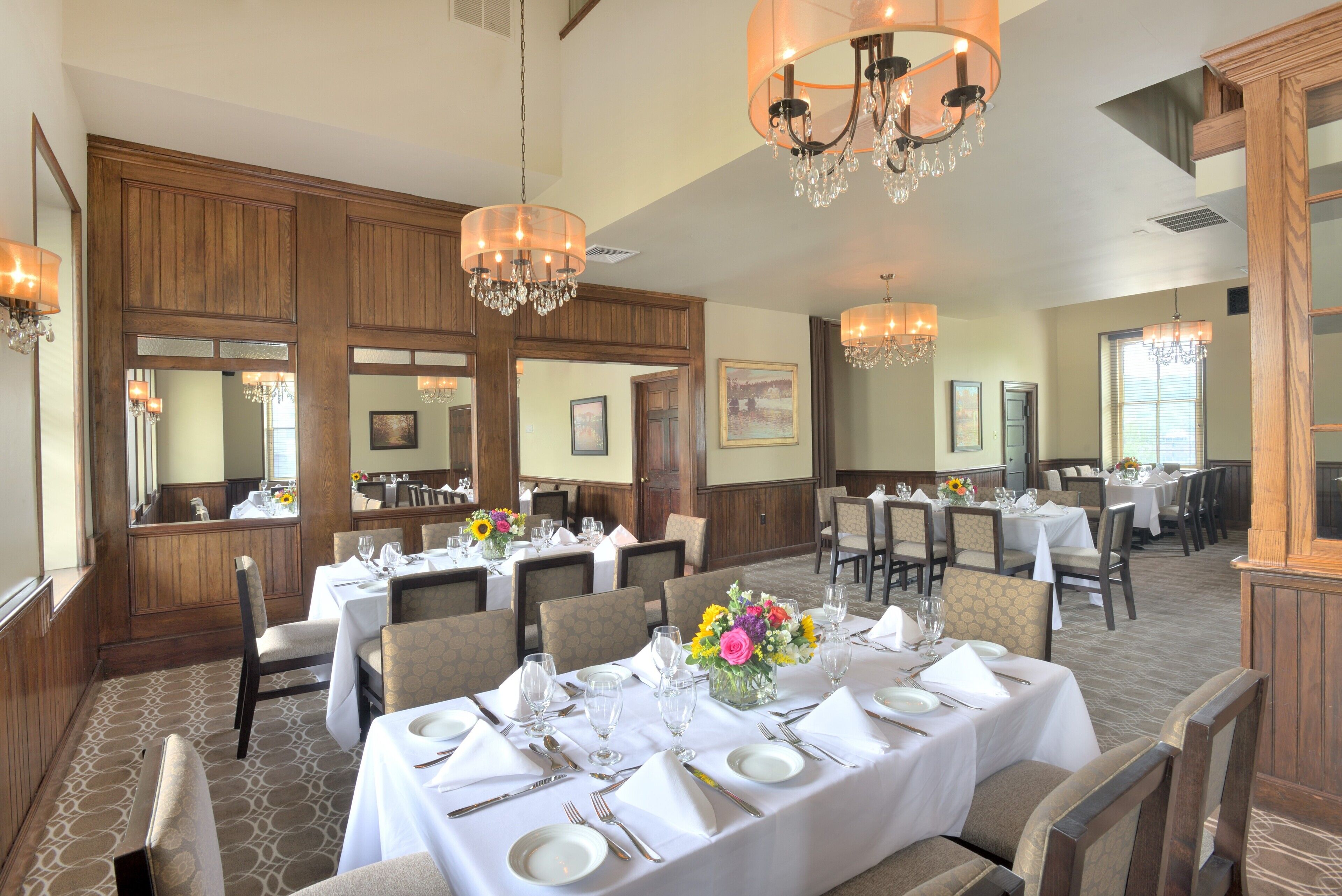 A dining area with tables set for service, chandeliers, and wooden paneling.
