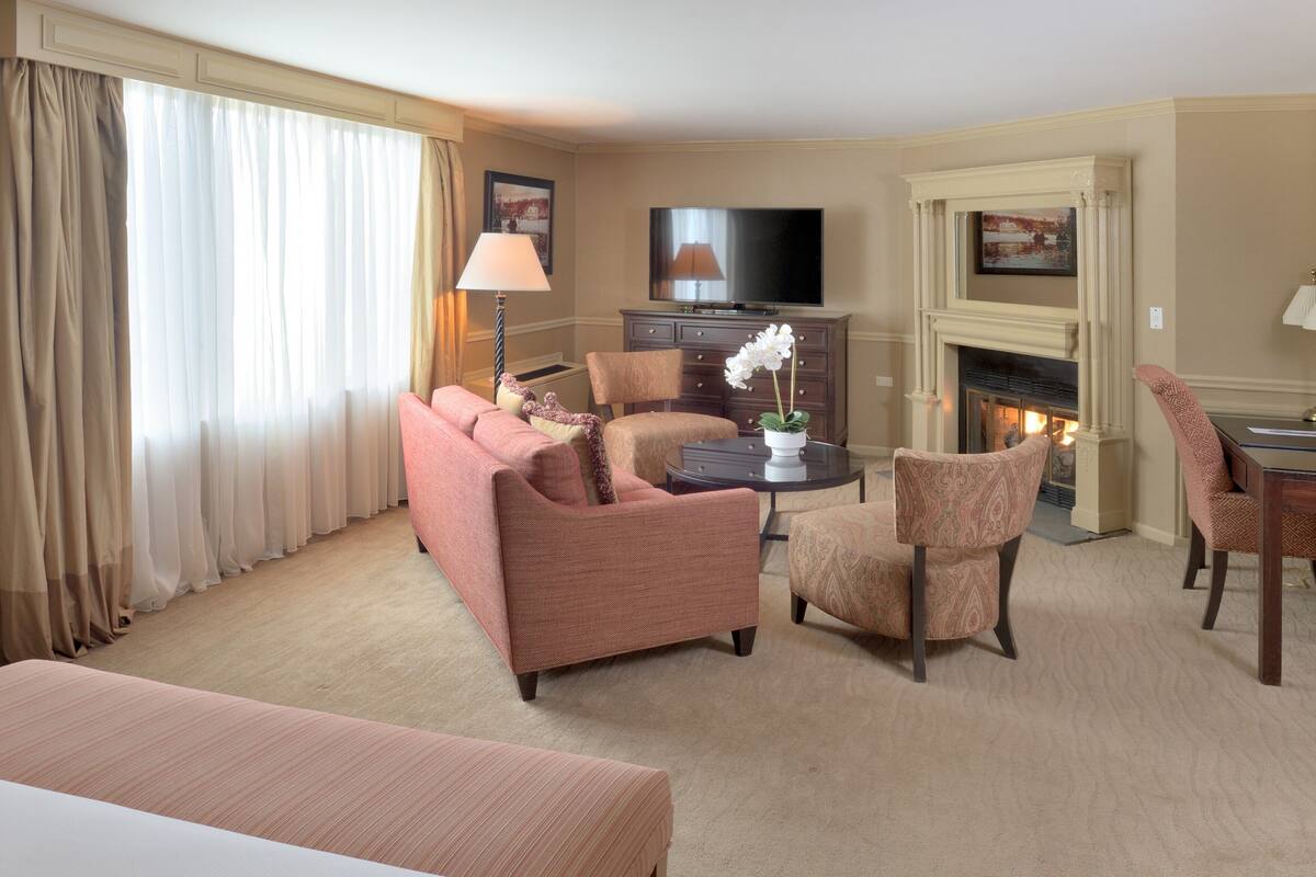 Ein Hotelzimmer mit Sofa, Sesseln, einem kleinen Tisch mit Lampe, einem Fernseher und einem Kamin.