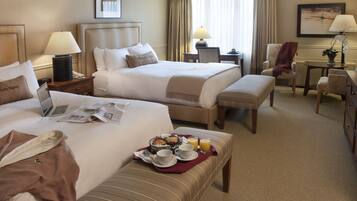 A hotel room with two beds, a desk, a chair, and a small table with a lamp.