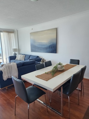 A modern living room with a white dining table, dark blue sofa, and a large abstract painting on the wall.