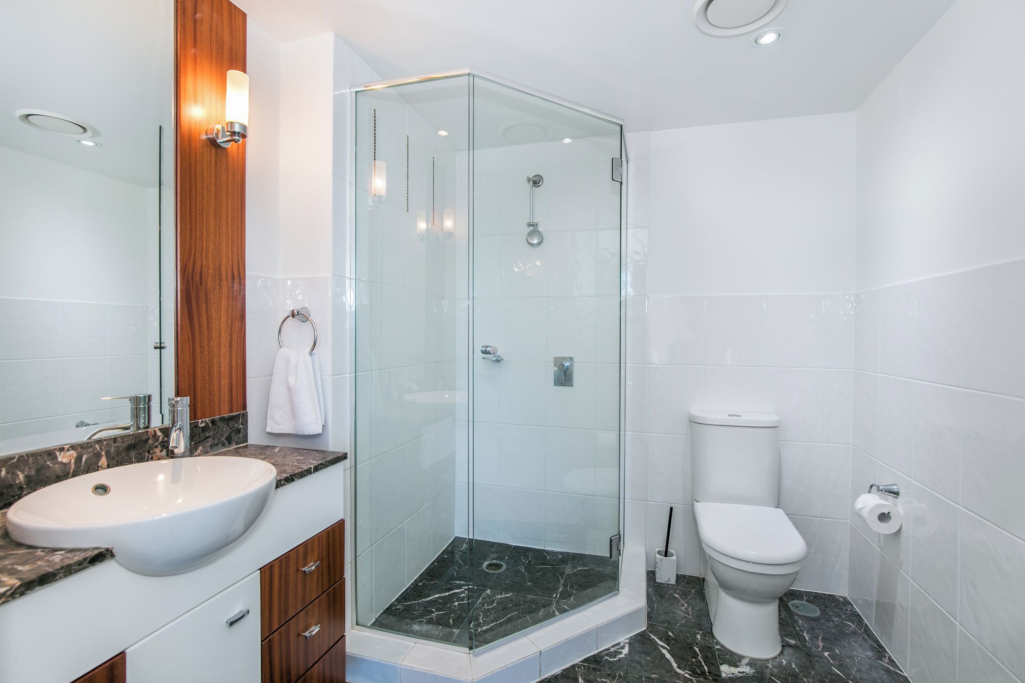 A modern bathroom with a glass-enclosed shower, a white sink, and a toilet.