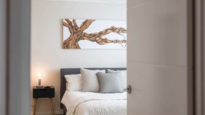 A bedroom with a bed, pillows, a nightstand with a lamp, and a wall-mounted artwork of a tree branch. - Summer Sky - Oceanstays (Yamba)